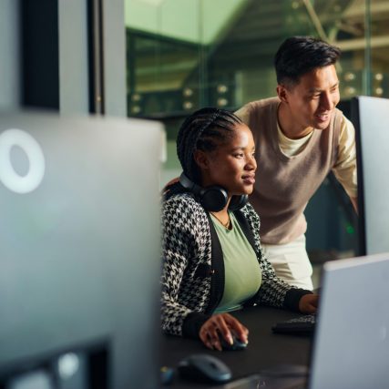 Software engineers collaborating on a project, analyzing code on computer monitors in office